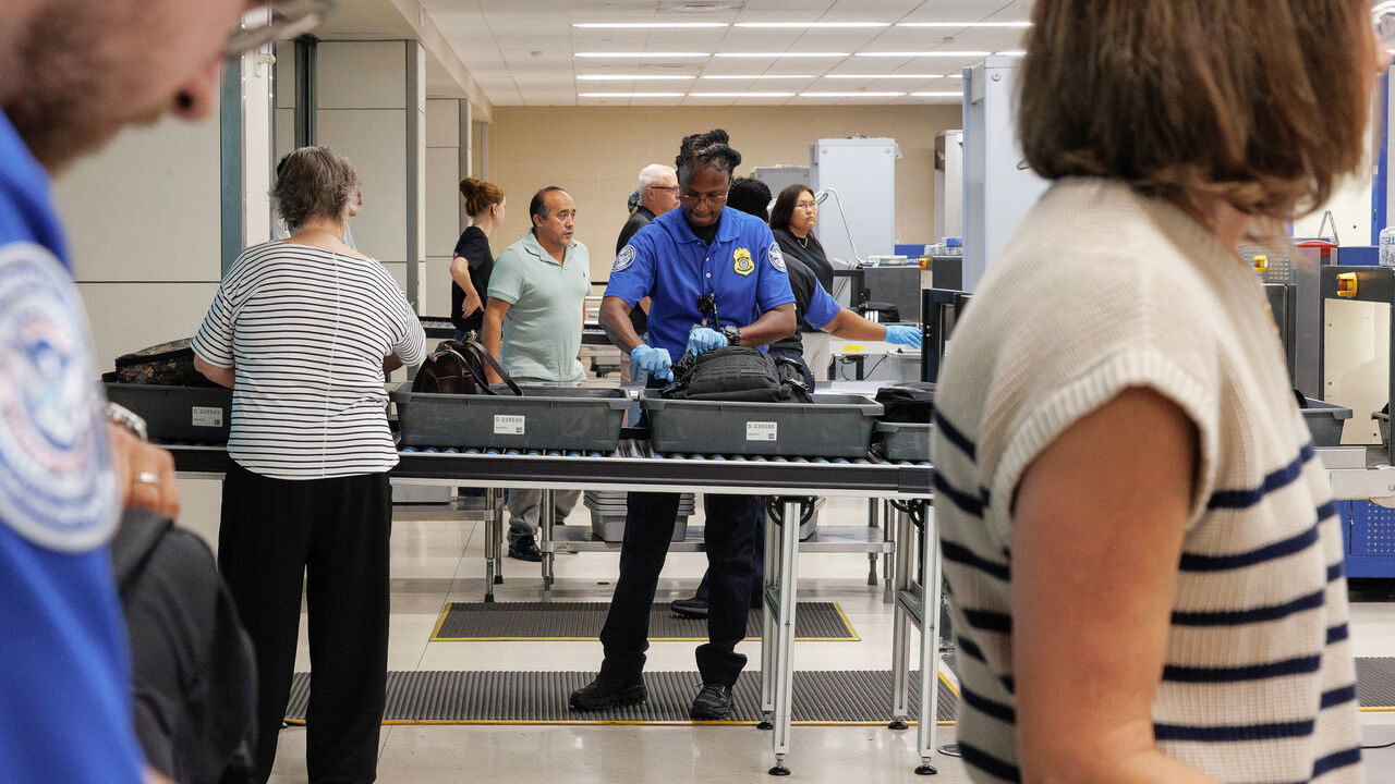 A Transportation Security Administration agent assists travelers as they place their luggage onto a scanner belt at the TSA security checkpoint.