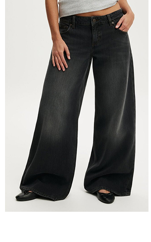 Woman wearing oversized black wide-leg jeans with ripped knee detail and gray crop top
