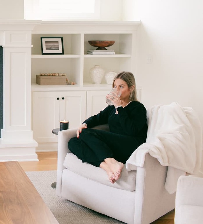 image of woman sitting in a chair drinking water with a candle lit next to her