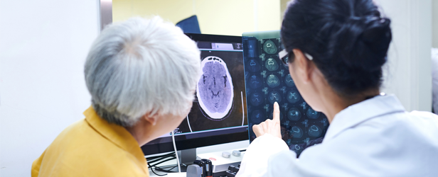 A doctor and a senior, female patient checking MRI film in an office.