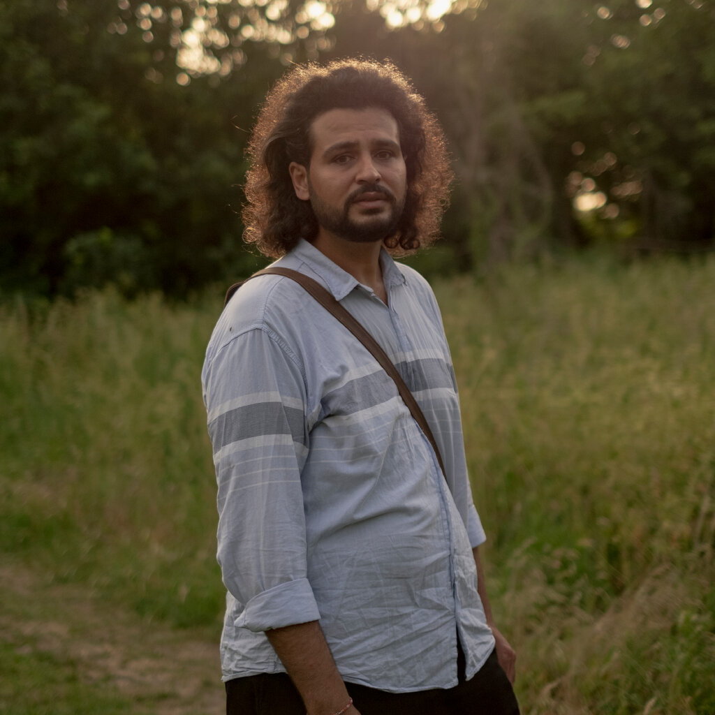A man with curly dark hair stands in a field.
