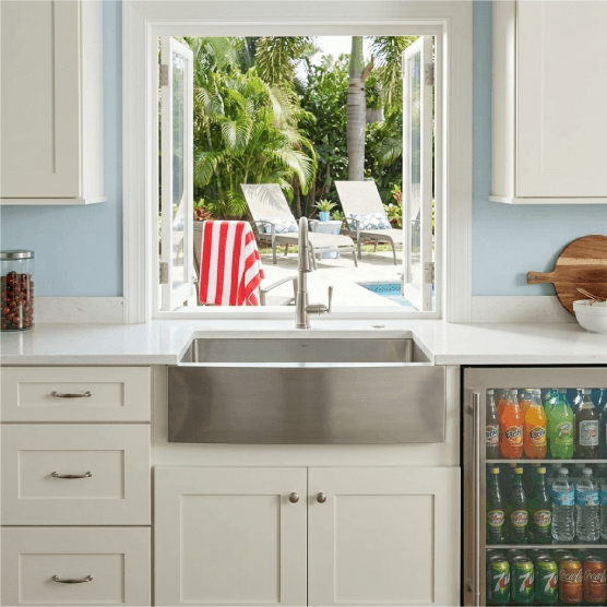 White Kitchen cabinets and sink with poolside view and open window.