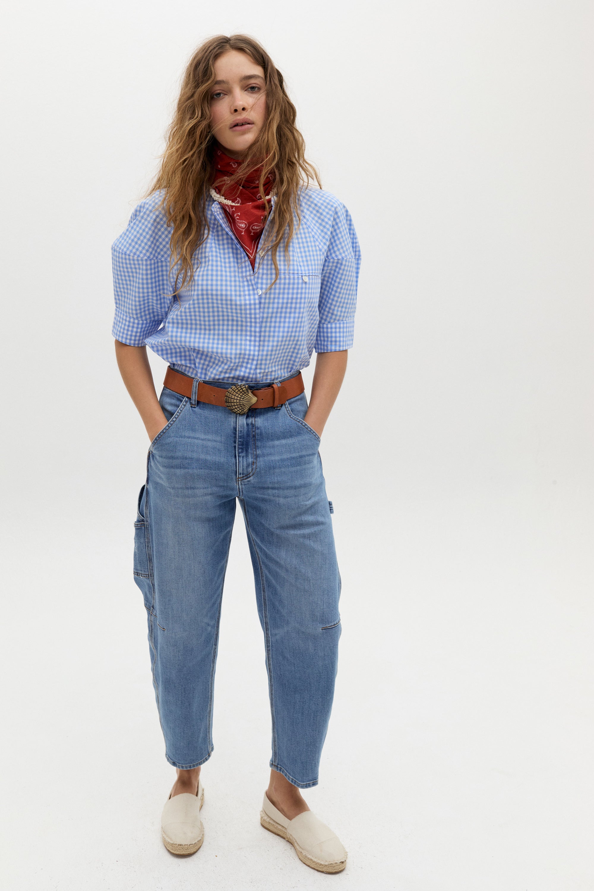 a woman standing in front of a white background wearing jeans