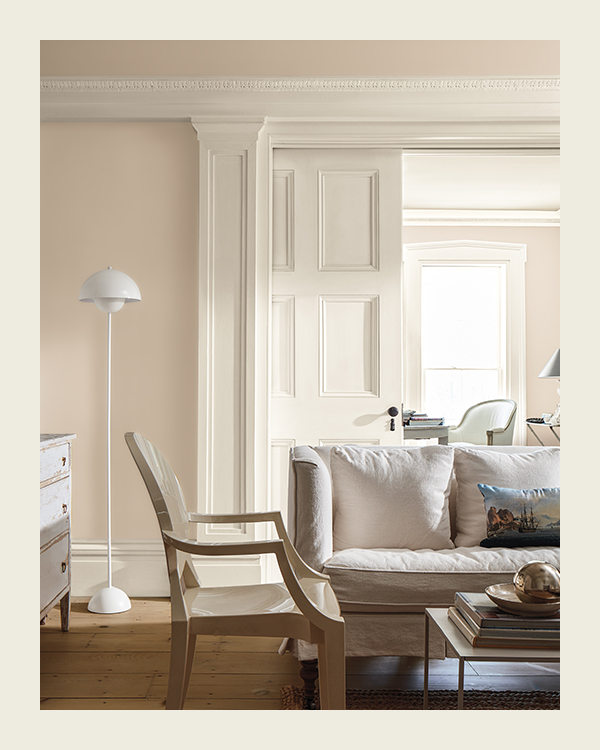 A living area with blush walls, white trim and doors, hardwood floors, an off-white sofa and chair, and a white floor lamp.