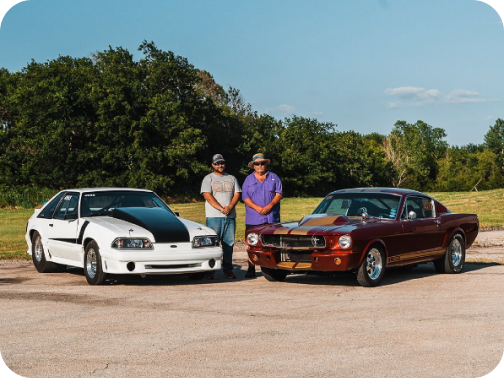 Two classic Ford Mustang&reg; fastbacks with their owners standing between them