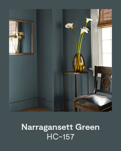 Narragansett Green HC-157 - A dark teal painted space with a vintage chair, mirror, and side table topped with a vase filled with white flowers.
