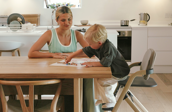 Image of Mother helping son who is drawing whilst sat in Nest & Nurture Highchair at kitchen table.
