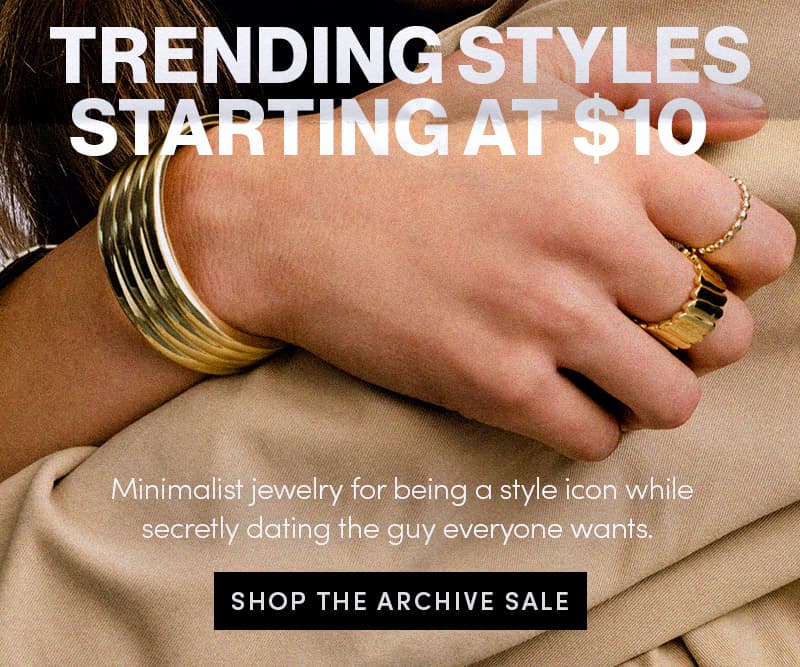 Hand wearing gold bracelet and rings over a beige coat