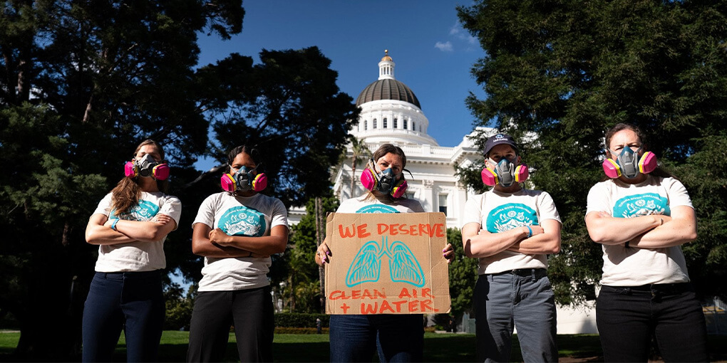 Activists pose in front of the state capitol in Sacramento wearing respirators.
