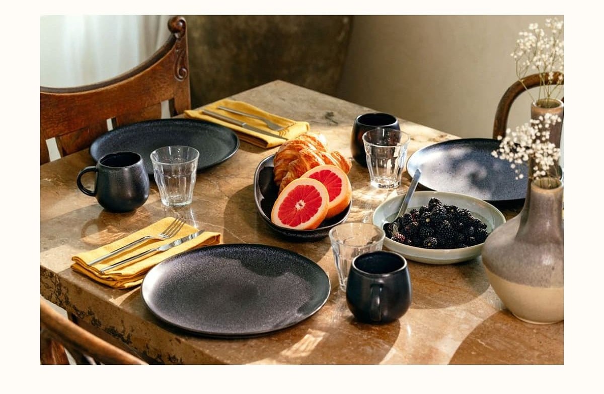 A table set with plates, glasses, fruit, and cutlery, suggesting a meal or gathering.