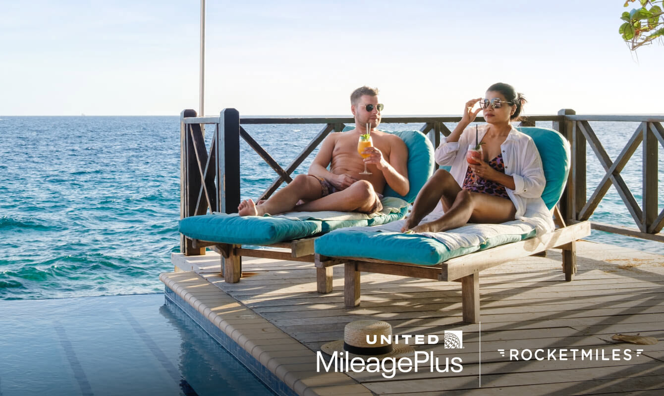Two people lounging on chairs waterside and enjoying drinks.