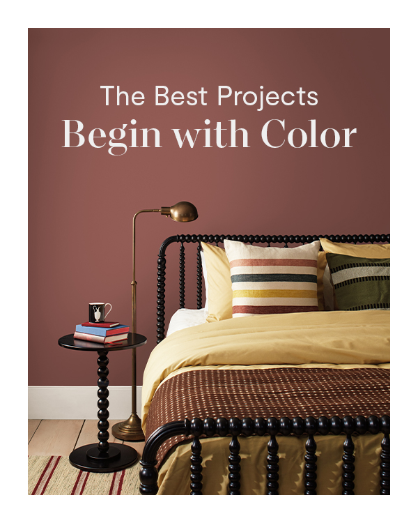 A bedroom with clay red walls, a black spindle-frame bed and side table, and cozy tan bedding with striped pillows.