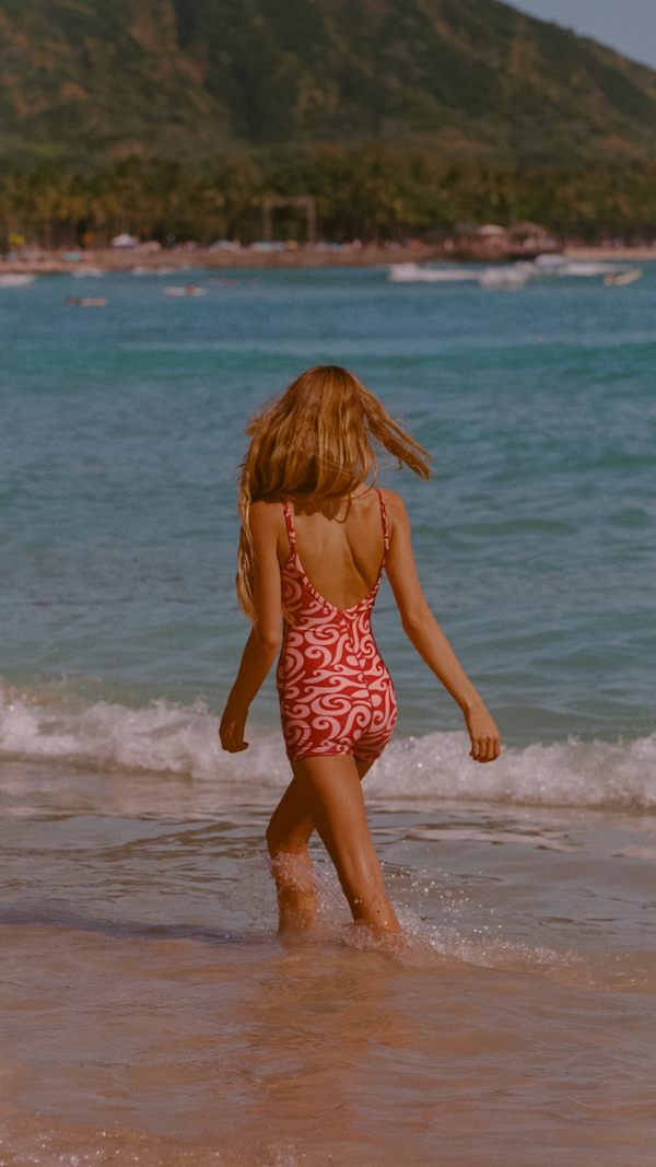 woman wearing a pink long jane wetsuit on the beach and a mask on forehead with shells inside