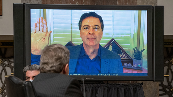 James Comey is seen on a monitor raising his right hand when being sworn in at a hearing on Capitol Hill.