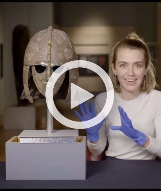 Curator sat next to the Sutton Hoo helmet.