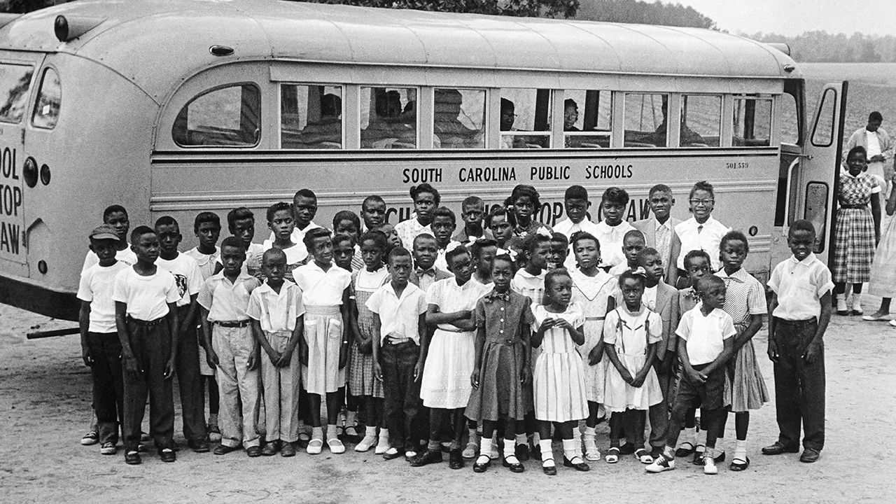 Black school children posing in front of a school bus in the 1950s