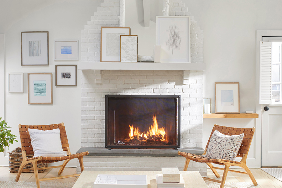 A white wall with framed artwork and white-painted brick fireplace flanked by matching leather and wood chairs.