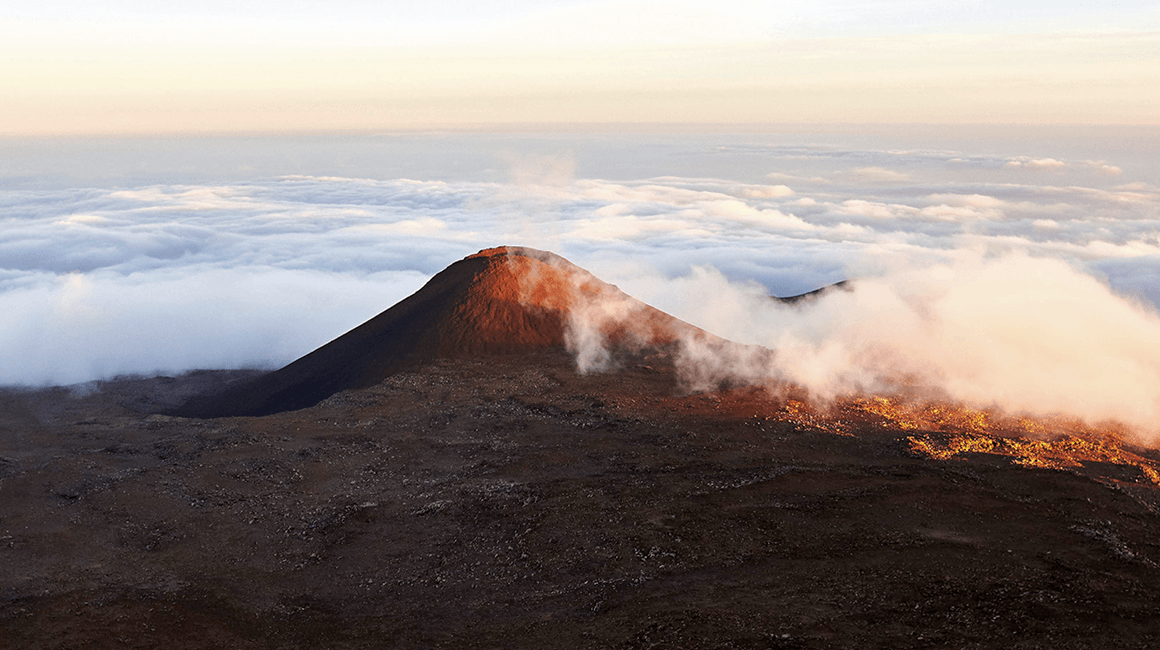 Steam rising around a dormant volcano at sunrise above the clouds.