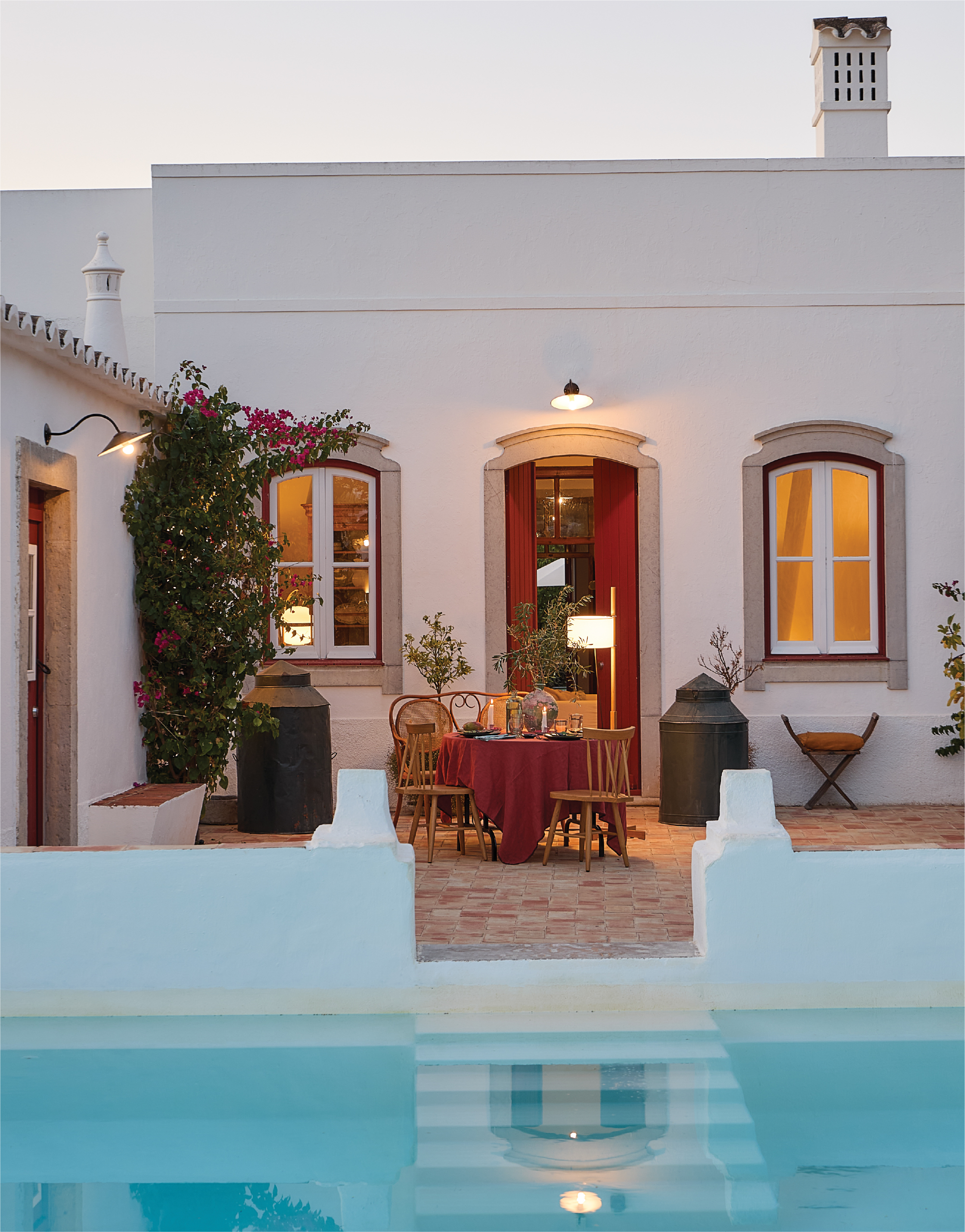 Table set with a red tablecloth on a terrace at dusk, next to a pool, in a traditional Portuguese country house