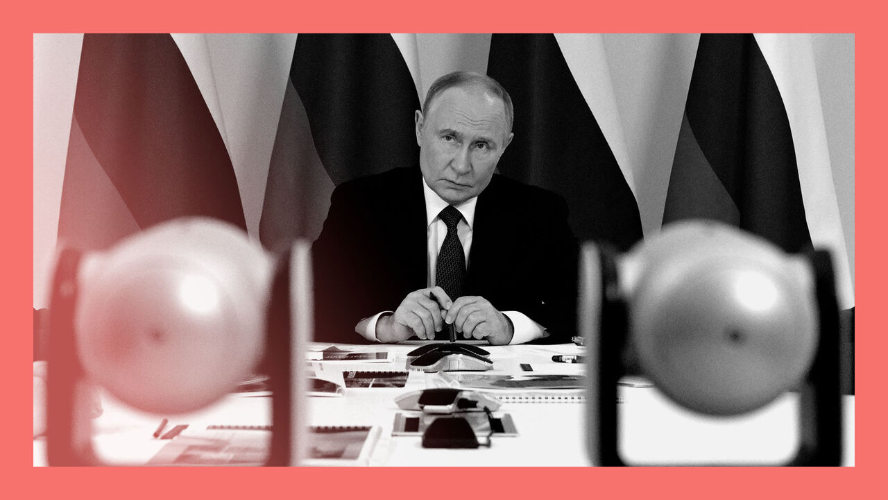 Russian President Vladimir Putin sits at a desk with Russian flags in the background as he attends a meeting during visiting to Magadan, on the way to Alaska.