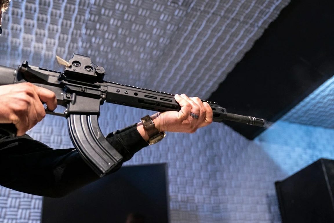 A person fires a semiautomatic rifle at an indoor shooting range, with smoke visible at the muzzle.