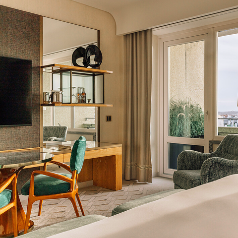 Refined guest room with desk, lounge chair, and balcony doors that open to city views.