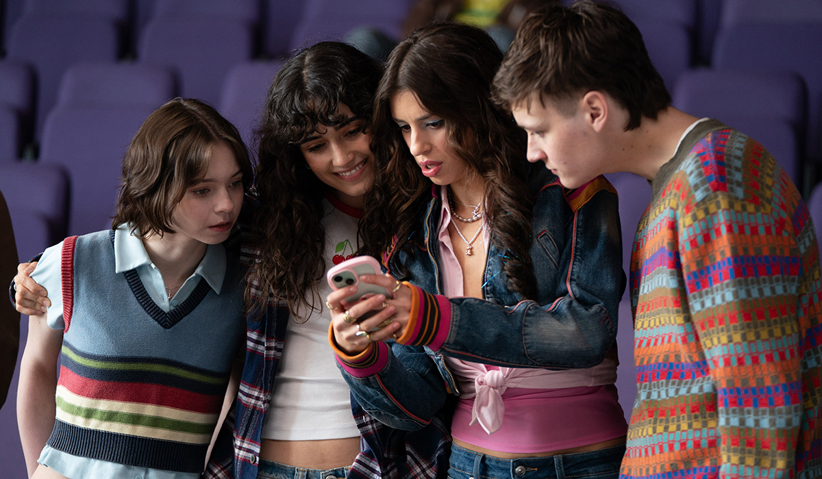 Three young women and a guy stand looking at a phone.