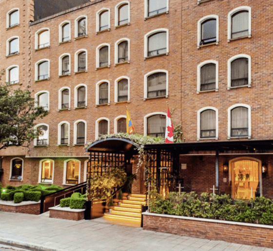 Brick building hotel entrance adorned with flags, surrounded by greenery.