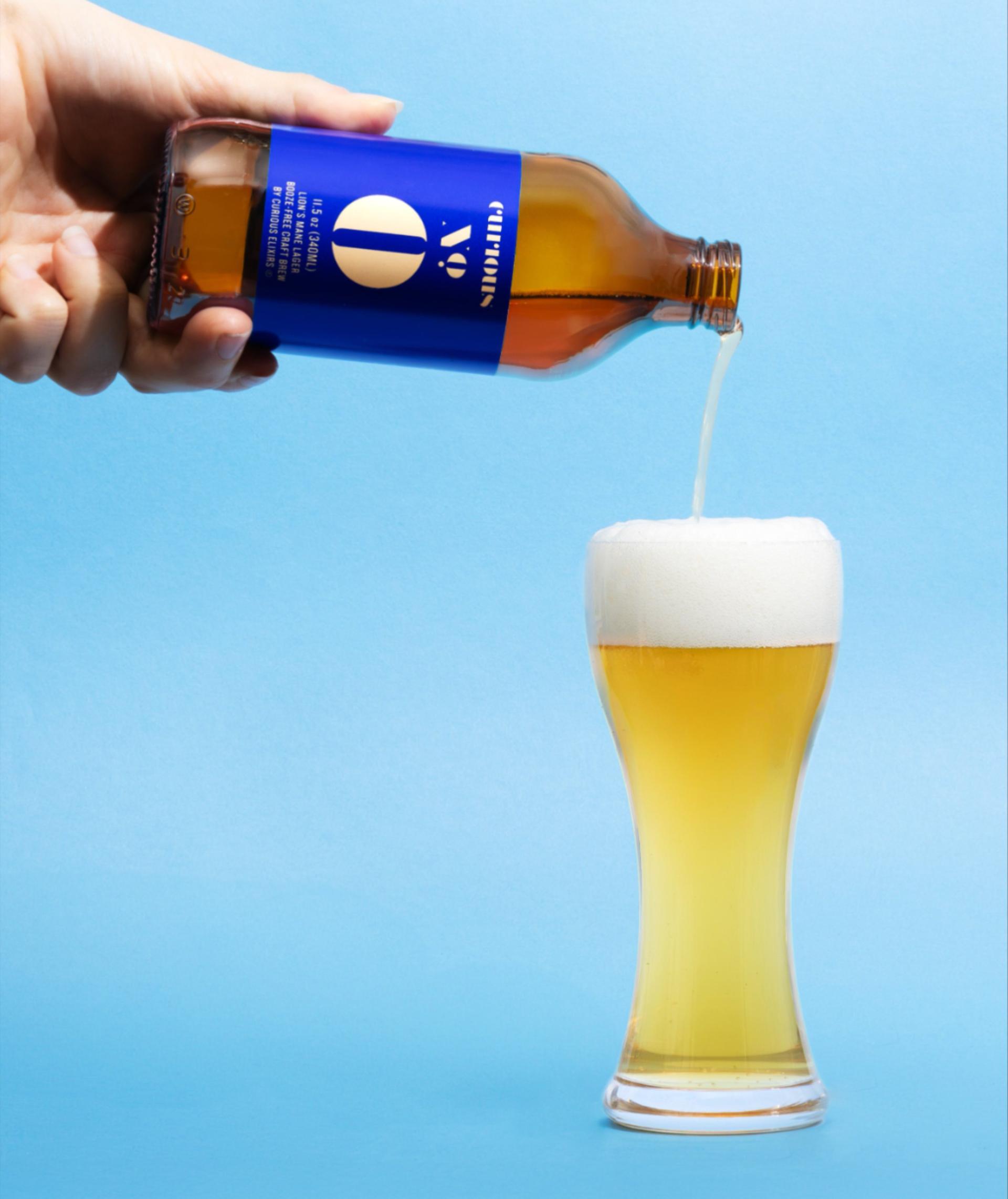 Curious Zero being poured into a beer glass on a light blue background