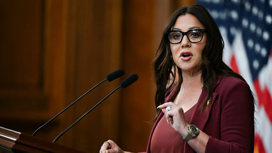 A woman speaks at a podium by an American flag.