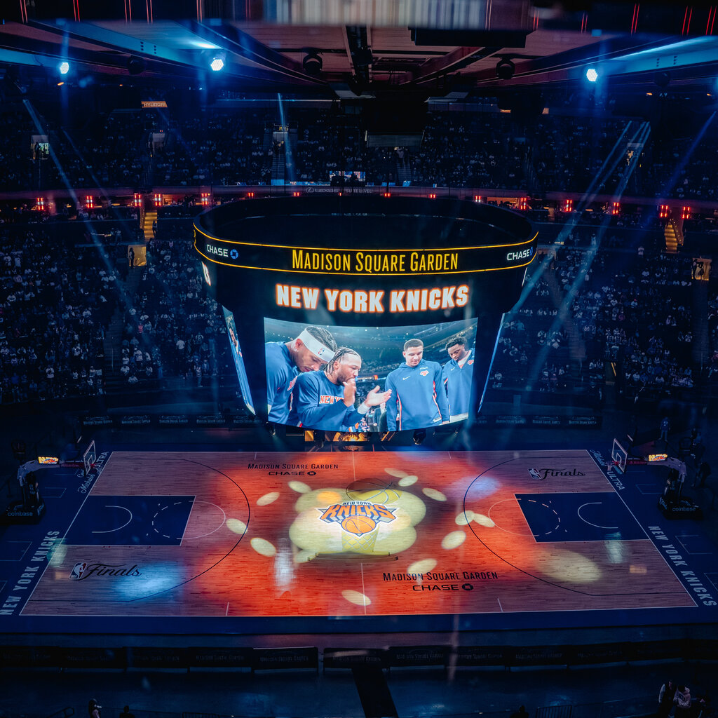 A group of basketball players seen on a large screen above the court at Madison Square Garden.