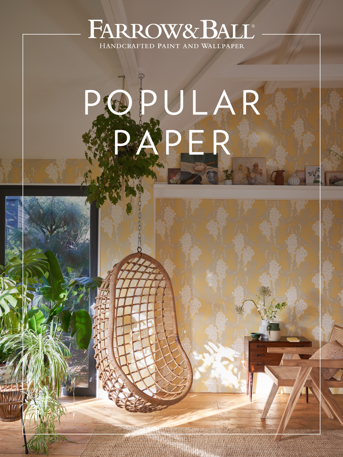 A sunny yellow floral wallpaper wraps this living space in light, highlighting natural textures, hanging greenery and wooden floors. The room has an uplifting atmosphere that feels both cheerful and relaxing.