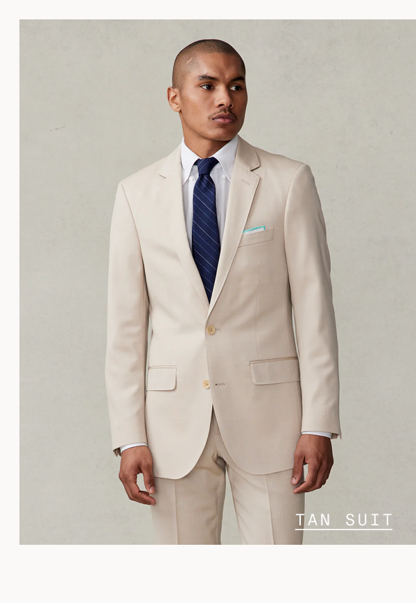 Bald man with a mustache looking off to the side, wearing a tan suit jacket over a white dress shirt with a navy striped tie and a light blue pocket square. TAN SUIT