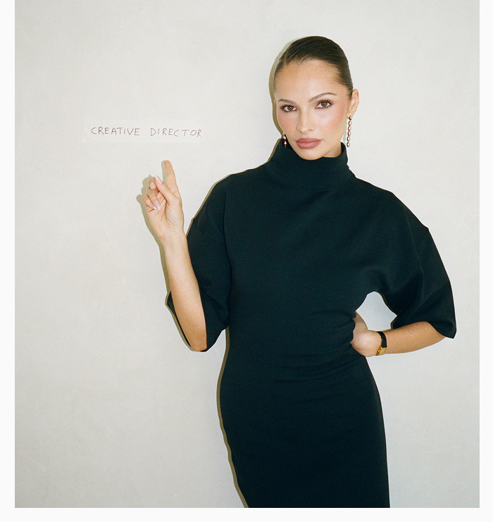 Heaven Mayhem founder, Pia Mance posing in front of white backdrop and pointing to handwritten 'CREATIVE DIRECTOR' written behind her.