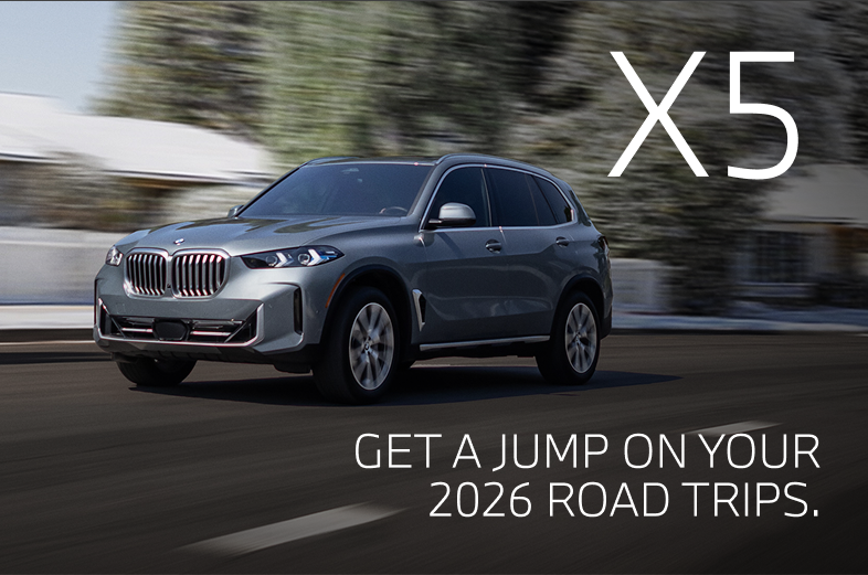 2026 BMW X5 driving down a winter road with snowy trees in the background
