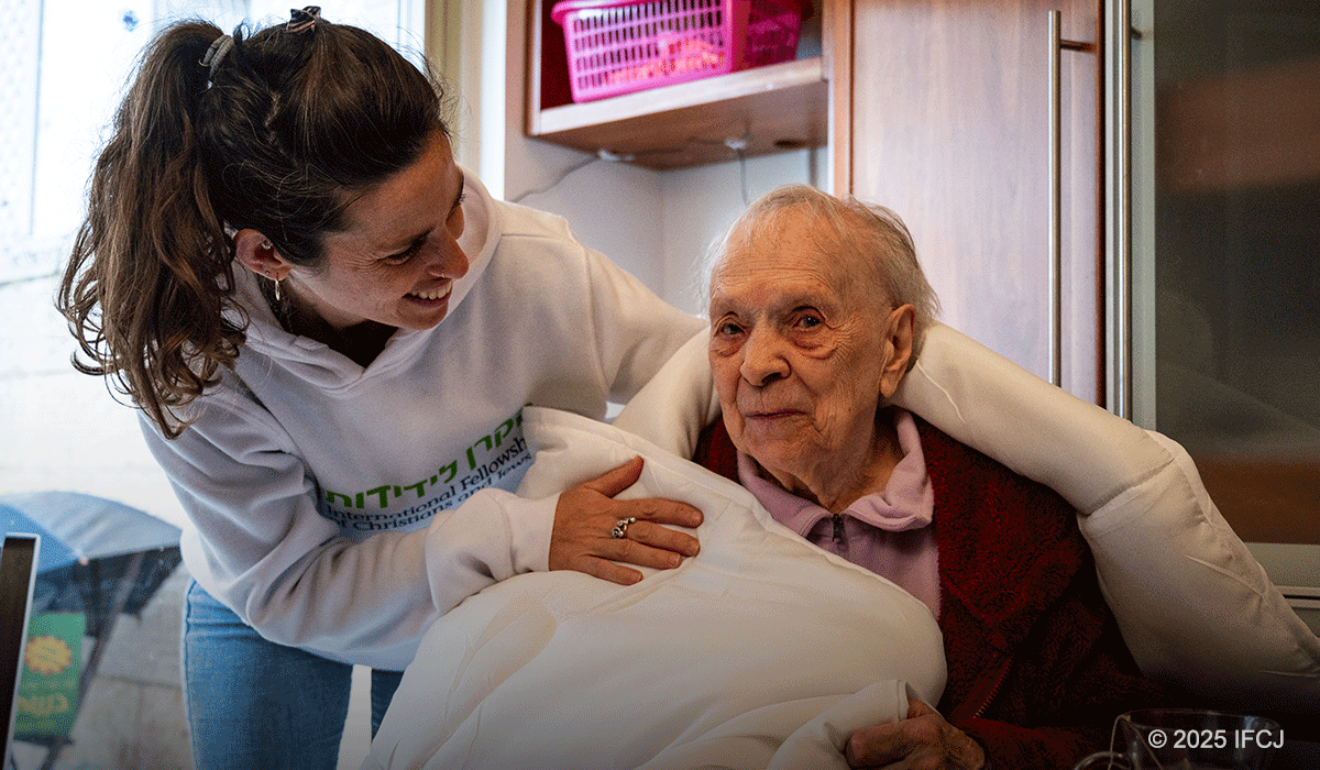 IFCJ staff member wrapping a white blanket around an elderly woman.