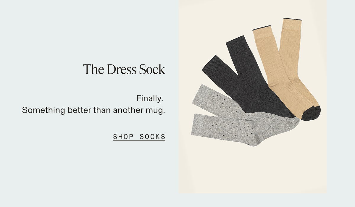 Three pairs of dress socks fanned out on a cream background — gray speckled, charcoal, and tan with black toe and heel — against a light blue panel. The Dress Sock. Finally. Something better than another mug. SHOP SOCKS