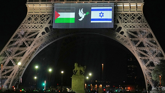  A sign hangs from the Eiffel tower where a dove is between a Palestinian flag and an Israeli flag.