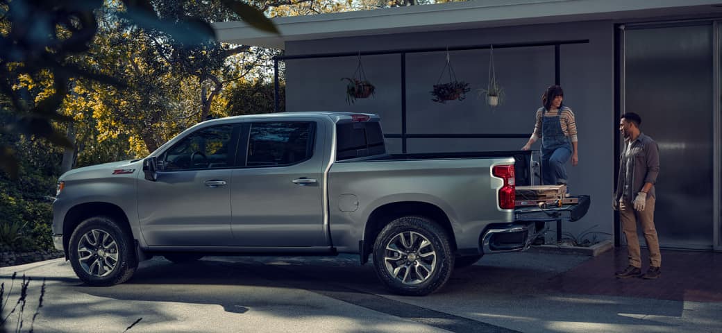Chevy truck parked in front of a house; two people stand by the bed loaded with wood planks.