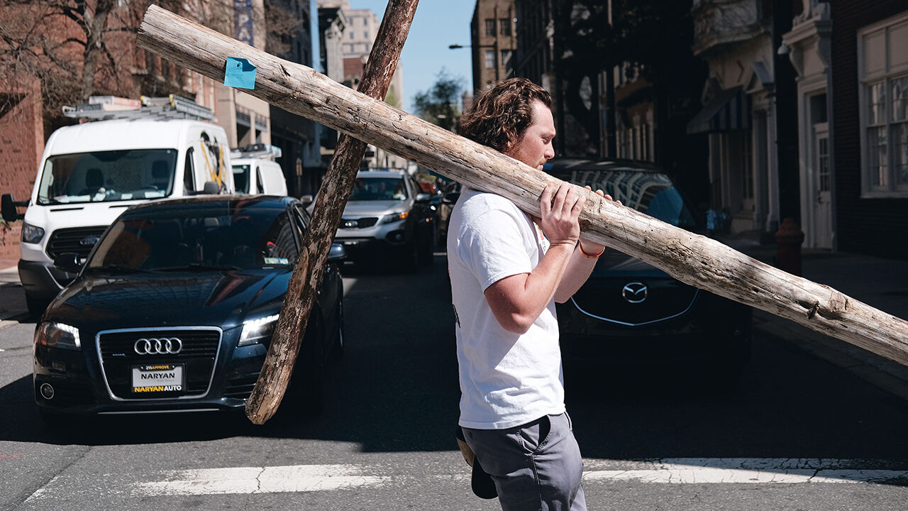 A teenage boy carries a large wooden cross through a street in Philadelphia, Pennsylvania