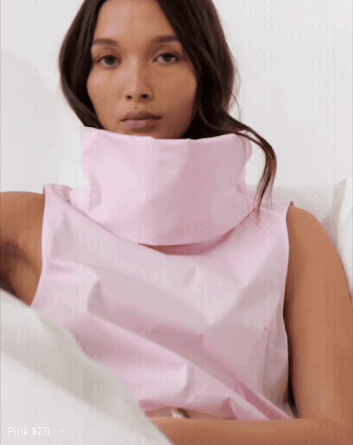 Yada reclines in the Marcy Sleeveless Top with a dramatic high collar, labeled “Pink $78.”