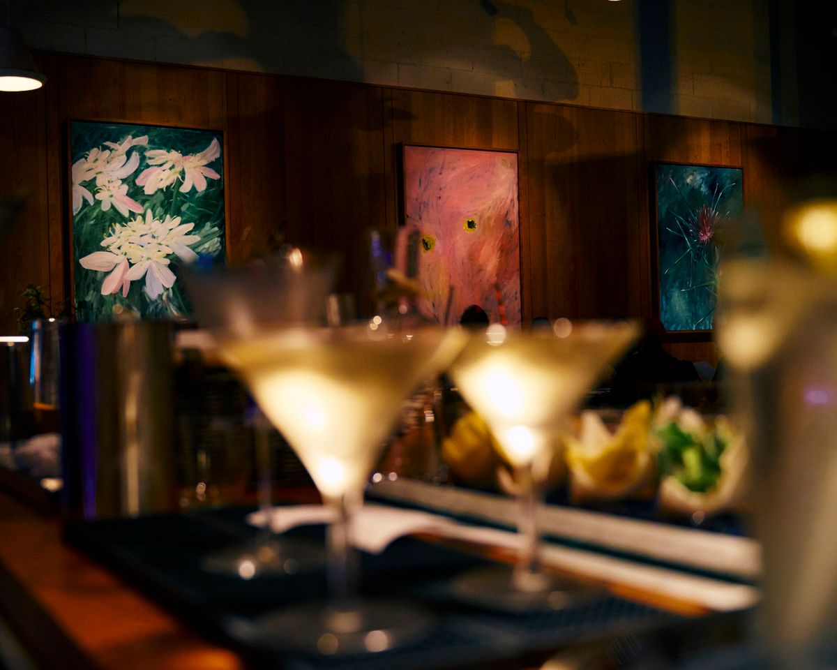 Filled Martini glasses at a bar table, with paintings on the wall in the background.