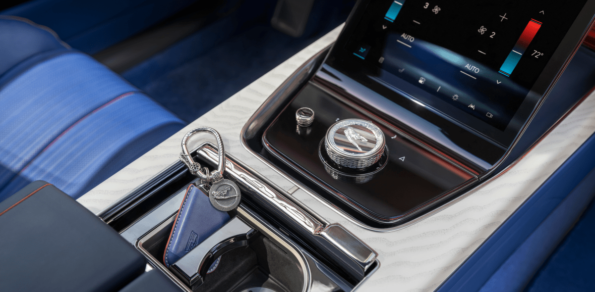 Cropped shot of the Cadillac CELESTIQ center console featuring a sleek touchscreen interface and a stylish key fob resting near the beverage holder, amidst sophisticated surrounding seats and surfaces.