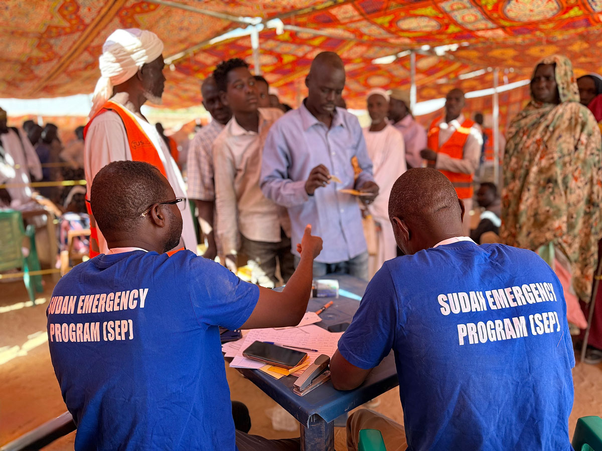 A group of people are standing in line by the emergency program staff.