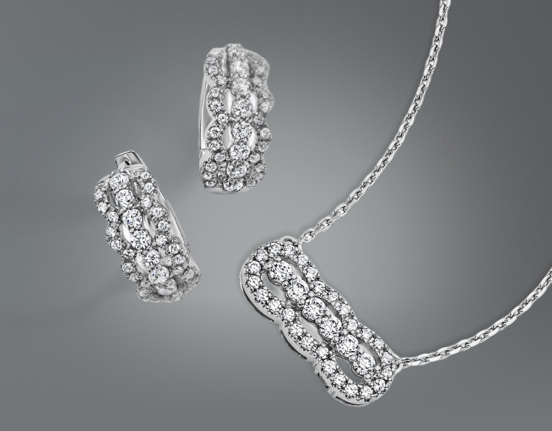 Two multi diamond earrings next to a necklace with a shimmering silver chain.