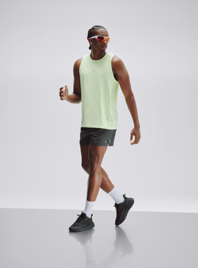 A man wearing a yellow running vest, black running shorts, trainers and running glasses