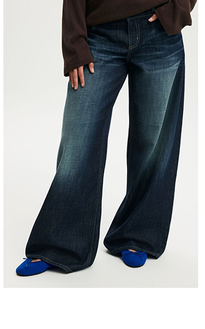 Model wearing dark blue wide-leg jeans with brown long-sleeve top and blue slippers