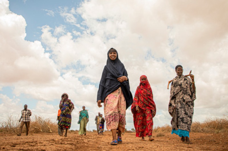 roup of women walking on a dry, dusty path under a cloudy sky.