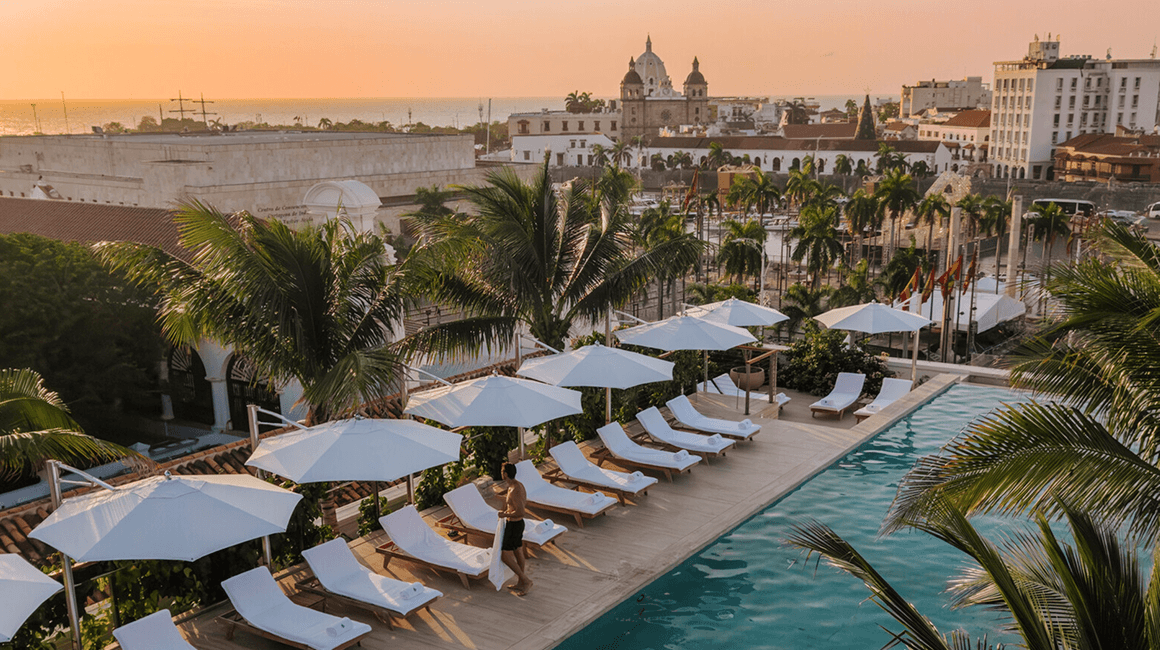 An outdoor pool lined with loungers and umbrellas, the city and ocean in the distance.