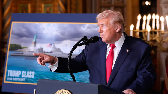 Trump stands in front of a poster of a battleship.